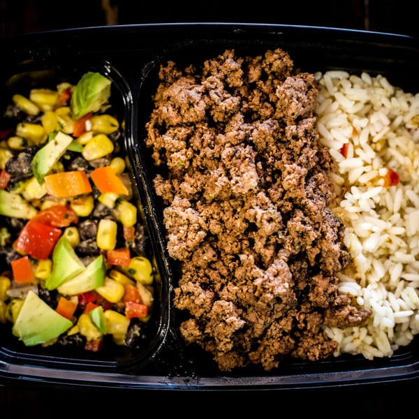 A meal prep container with ground beef, white rice, and a corn and avocado salad.