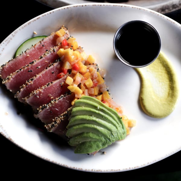 Seared tuna with sesame seeds, mango salsa, sliced avocado, and a side of soy sauce.