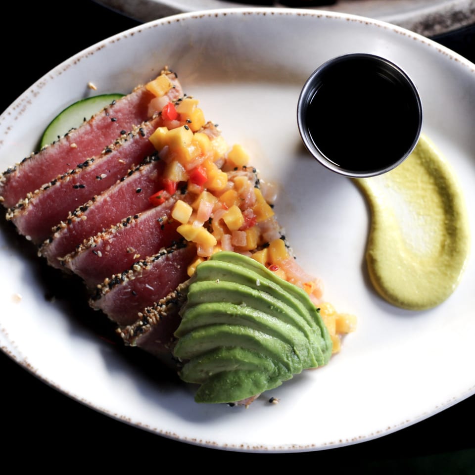 Seared tuna with sesame seeds, mango salsa, sliced avocado, and a side of soy sauce.
