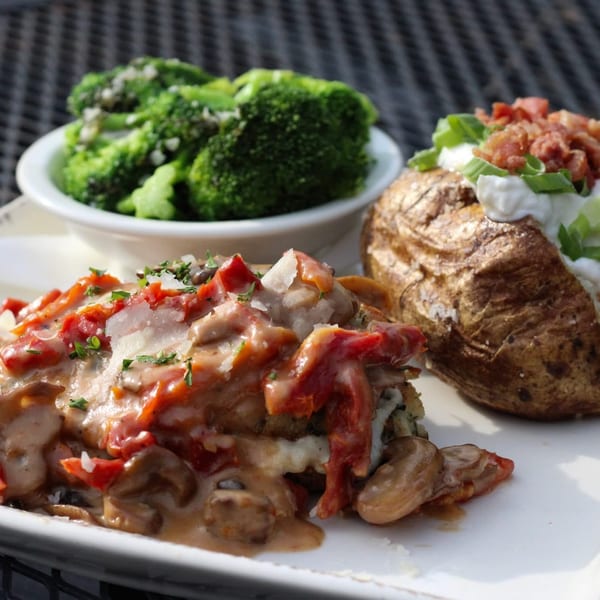 Chicken with creamy sauce, roasted red peppers, mushrooms, a baked potato, and broccoli.