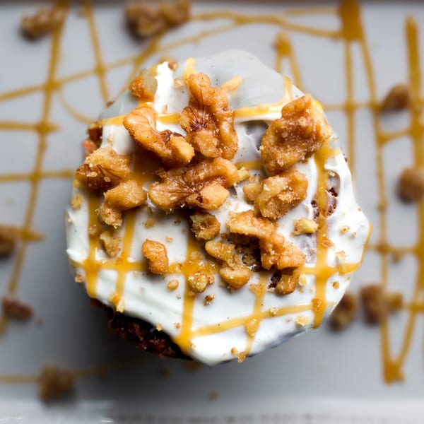Overhead view of a cupcake with white frosting, caramel drizzle, and candied walnuts.