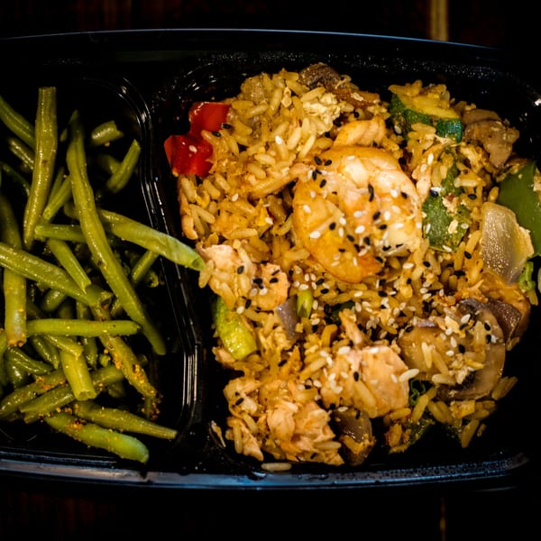 Shrimp and chicken fried rice with green beans in a black to-go container.
