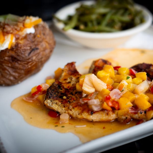 Grilled chicken with mango salsa, a loaded baked potato, and green beans on a white plate.