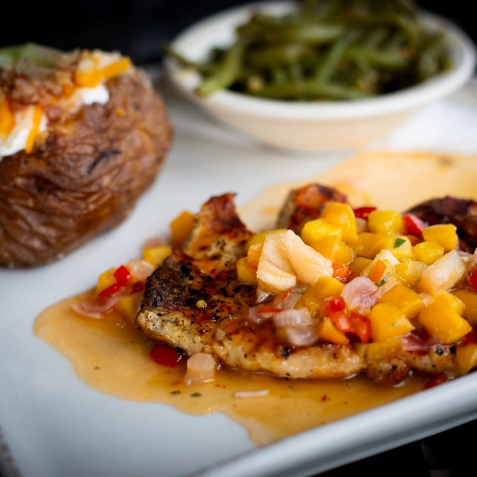 Grilled chicken with mango salsa, a loaded baked potato, and green beans on a white plate.