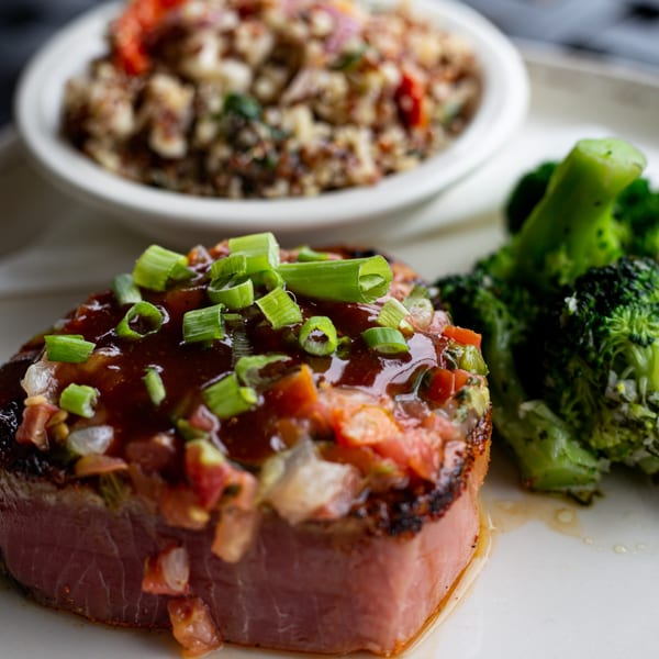 Seared tuna steak with sauce, chopped scallions, and pico de gallo, served with broccoli and quinoa.