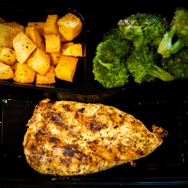 Grilled chicken breast, roasted sweet potatoes, and steamed broccoli in a black meal prep container.